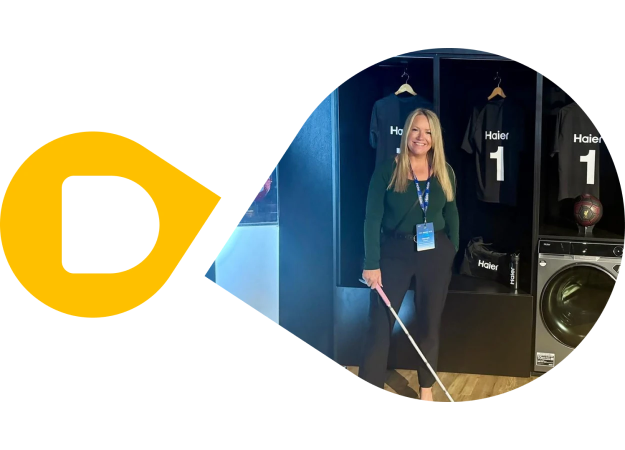 A photo of Hannah at the Haier showroom. She has long blonde hair and she's wearing black trousers and a dark green jumper. She's also carrying a cane